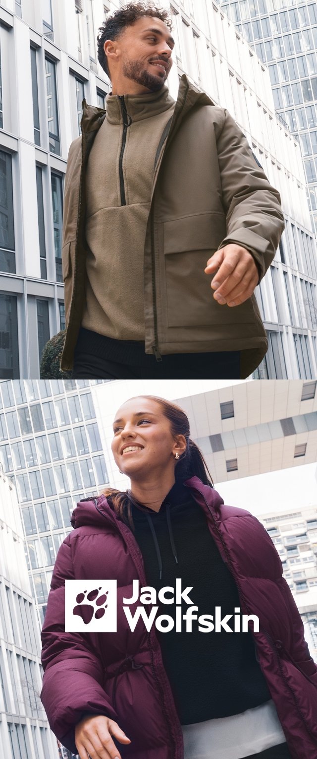Homme souriant en veste olive et femme en manteau matelassé violet marchant en plein air dans un environnement urbain avec des bâtiments modernes en verre.