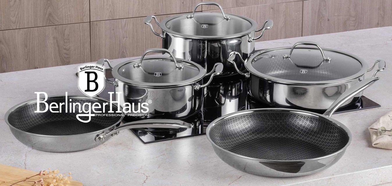 Pět nerezových hrnců a pánví s pokličkami ze skla uspořádaných na mramorové kuchyňské pracovní ploše poblíž sporáku a dekorativní vázy.