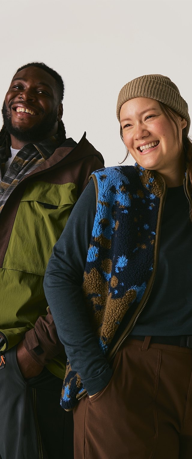 Dos modelos están juntos. Uno lleva una chaqueta verde y marrón, mientras que el otro viste un chaleco de forro polar azul y marrón con un patrón floral.