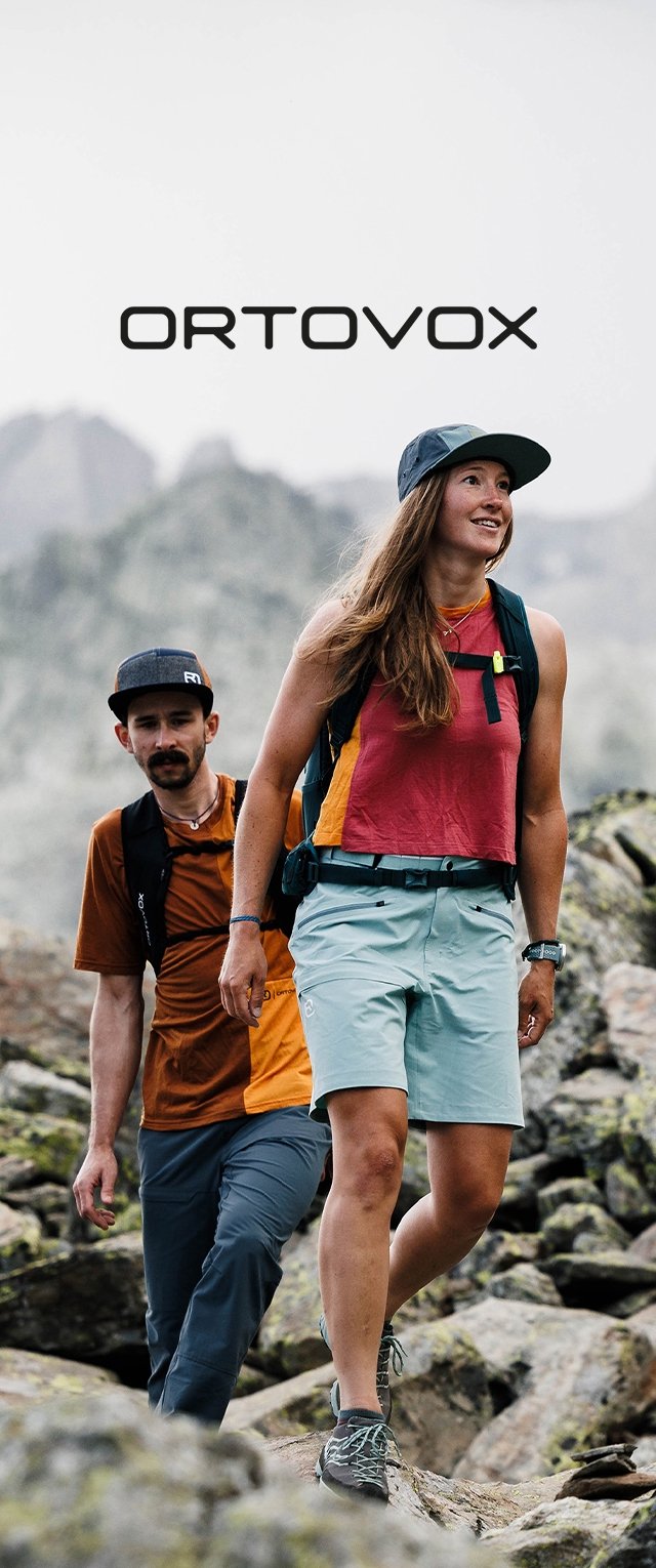 Due escursionisti su un terreno roccioso. La donna indossa una canotta rosa, pantaloni corti blu chiaro e un cappellino scuro. L'uomo indossa una maglietta arancione e pantaloni corti scuri.