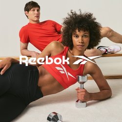 Dva mladí lidé v červeném sportovním oblečení cvičí; žena drží činku vleže na podlaze, muž se opírá o dřevěnou lať.