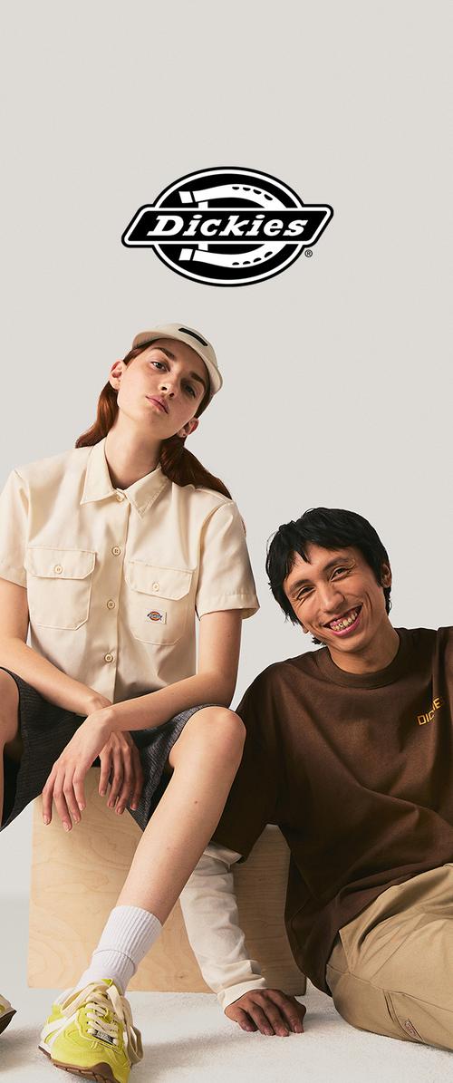 Divi modeļi, valkājot ikdienas Dickies apģērbu, sēž pie vienkārša fona ar Dickies logotipu virsū.