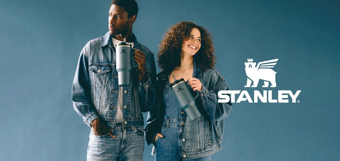 Muž a žena v džínových outfitech, každý držící šedý izolační termohrnek, stojí před modrým pozadím.