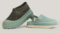 Zwei UGG Slipper: einer dunkelbraun mit dicker mintfarbener Sohle, einer hellblau mit offenem Fersenbereich und beiger Sohle, beide für den Freizeitstil gestaltet.