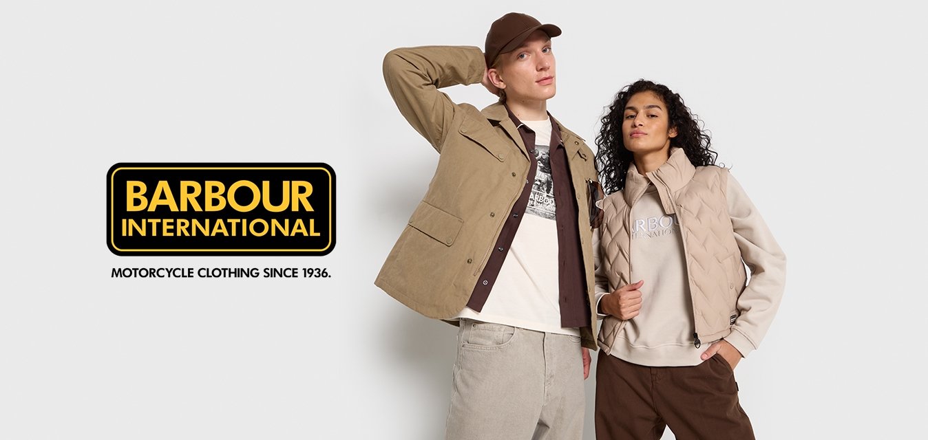 Muž v béžové bundě a kšiltovce s rukou za hlavou, žena v béžové vestě a mikině s rukou v kapse, oba stojící na bílém pozadí.