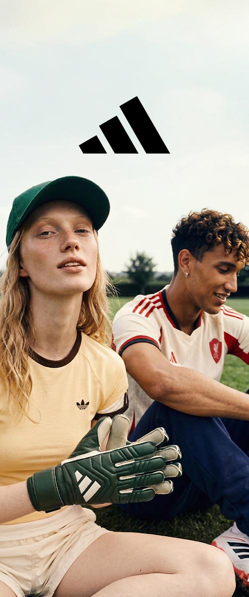 Jeune femme en tenue de sport et gants assise à côté d'un homme en maillot de football sur l'herbe avec le logo Adidas au-dessus d'eux.