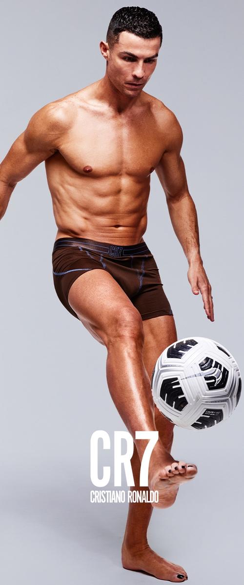 Braune Sportshorts mit blauen Akzenten, die eine muskulöse männliche Figur zeigen, die einen schwarz-weißen Fußball dribbelt.