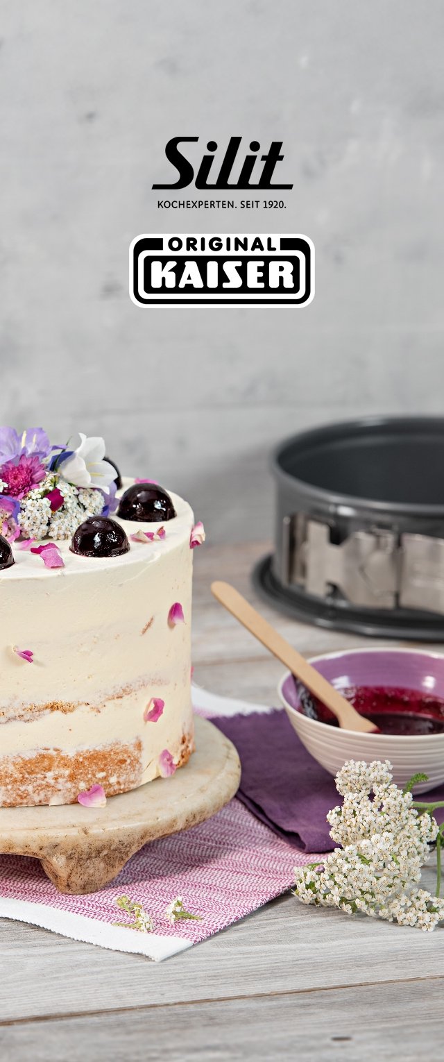 Runder Kuchen auf einem Marmorständer, dekoriert mit Sahne, lila Blumen und dunklen Kirschen. Begleitet von einer Schüssel Marmelade und einem Holzlöffel.