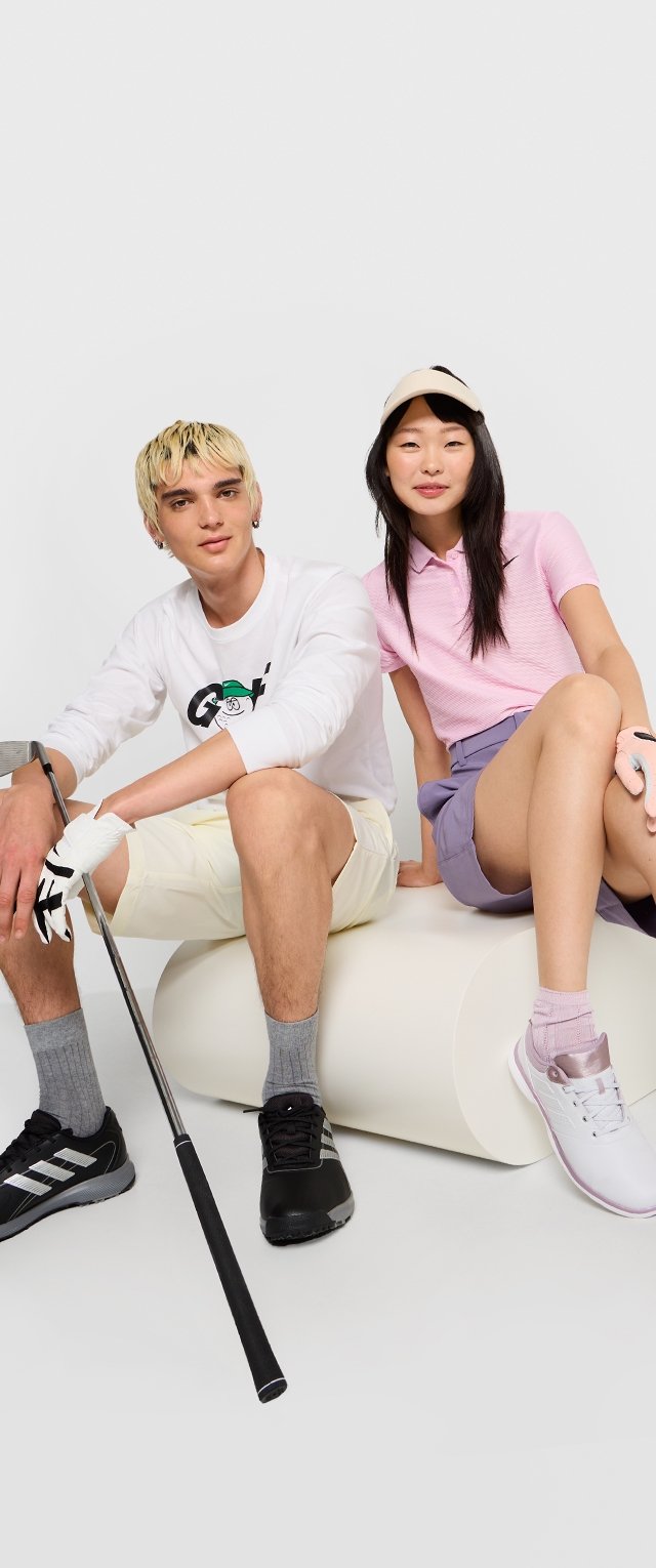 Zwei Personen sitzen auf einer gebogenen weißen Plattform. Die Person links trägt ein weißes Langarmshirt und gelbe Shorts und hält einen Golfschläger. Die Person rechts trägt ein pinkes Polo und lavendelfarbene Shorts und hält einen Golfball. Beide haben Sportschuhe an.