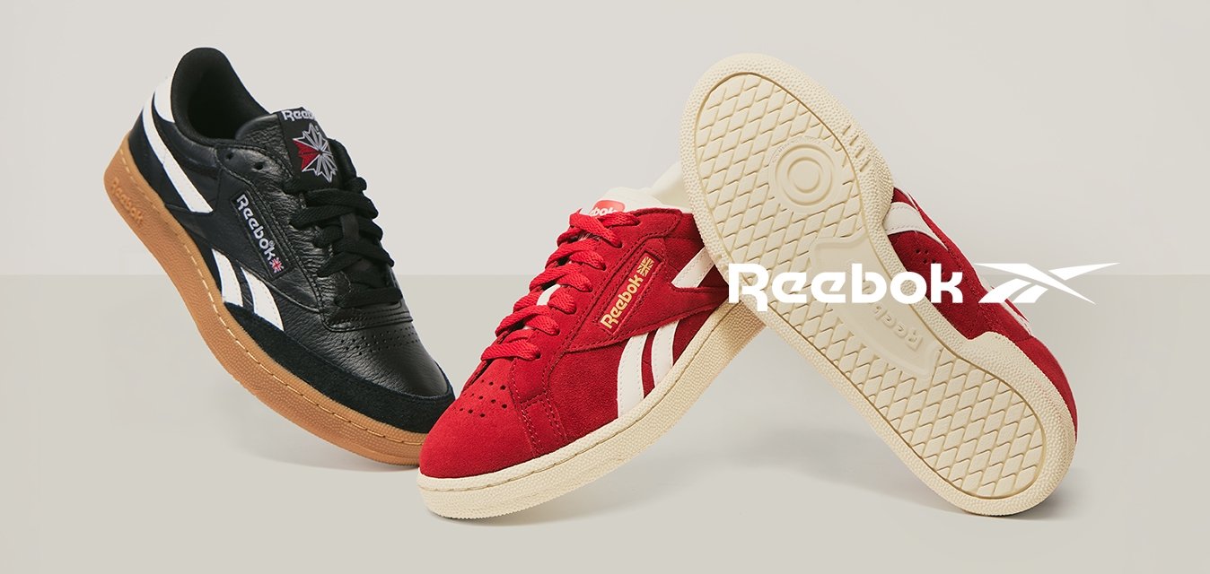 Černé kožené a červené semišové tenisky Reebok zobrazené vedle sebe, jedna červená bota ukazuje podešev s texturovaným vzorem.