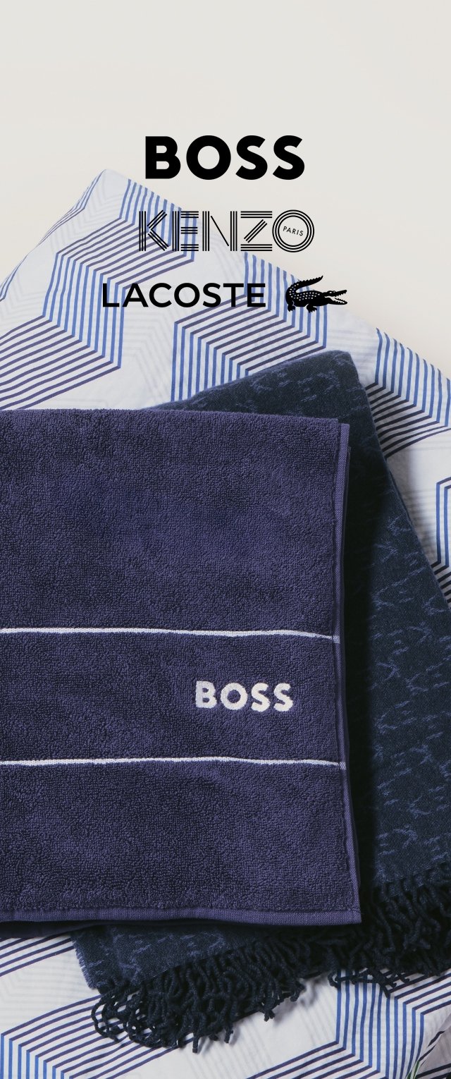 Ein Stapel aus drei gefalteten Handtüchern auf gemustertem Stoff; das oberste Handtuch ist dunkelblau mit "BOSS" in weißen Buchstaben bestickt.