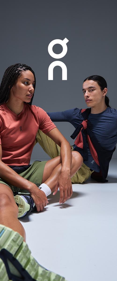 Sportbekleidung mit einem korallfarbenen T-Shirt und olivgrünen Shorts, sowie einem marineblauen Langarmshirt, auf einem grauen Hintergrund.