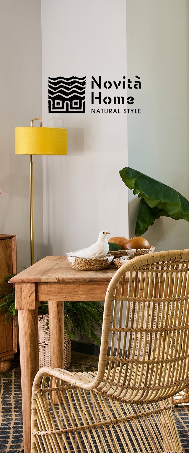 Houten tafel met een lichtbruine afwerking, rieten stoel, gele vloerlamp, potplanten en een decoratieve vogel in een geweven mand.