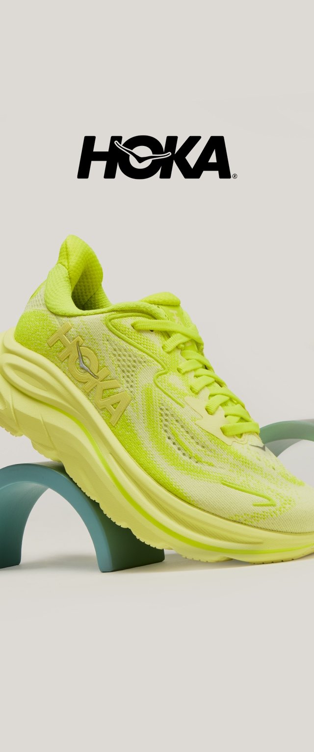 Spilgti dzeltena HOKA skriešanas apava pacelta uz izliekta zilā statīva ar HOKA logotipu virsū, uz gaiši pelēka fona.