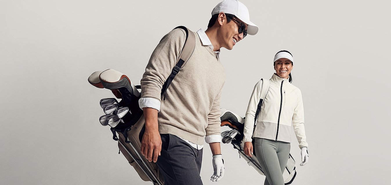 Muž a žena kráčejí nesoucí golfové tašky, oblečeni ve sportovním golfovém oblečení a čepicích, na jednobarevném světlém pozadí.