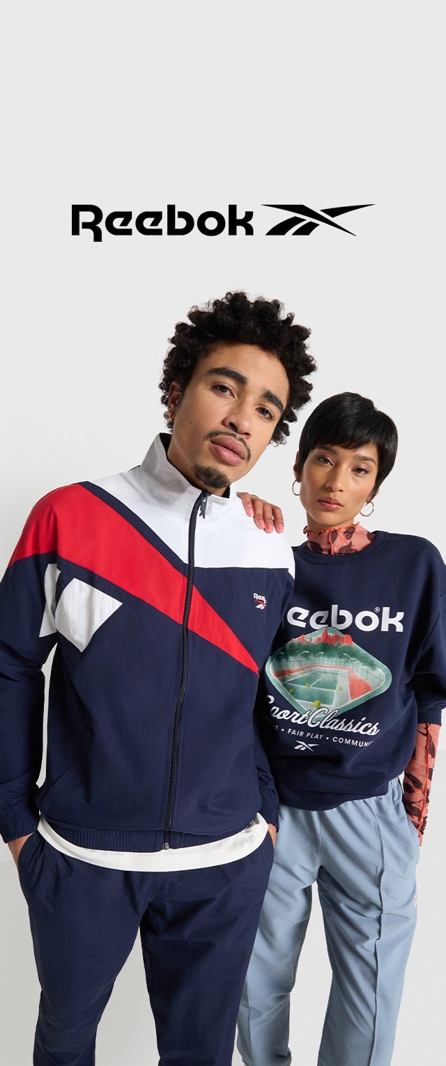 Chaqueta de pista Reebok en navy, rojo y blanco con cremallera; combinada con una sudadera navy con un diseño gráfico. Ambos modelos llevan pantalones a juego.