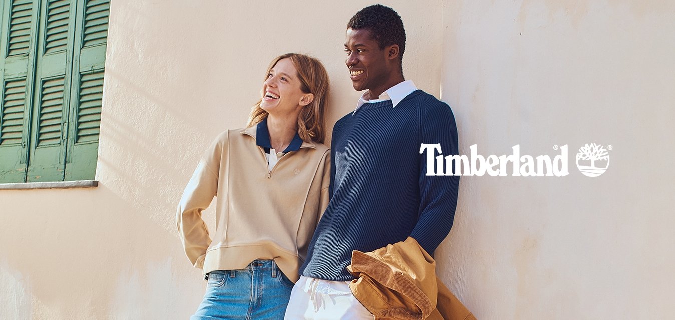 Béžový svetr na zip s modrým límečkem; námořnicky modrý žebrovaný svetr; světle modré džíny; hnědé boty; bílé kalhoty; hnědá bunda; texturovaná zeď; zelené okenice.