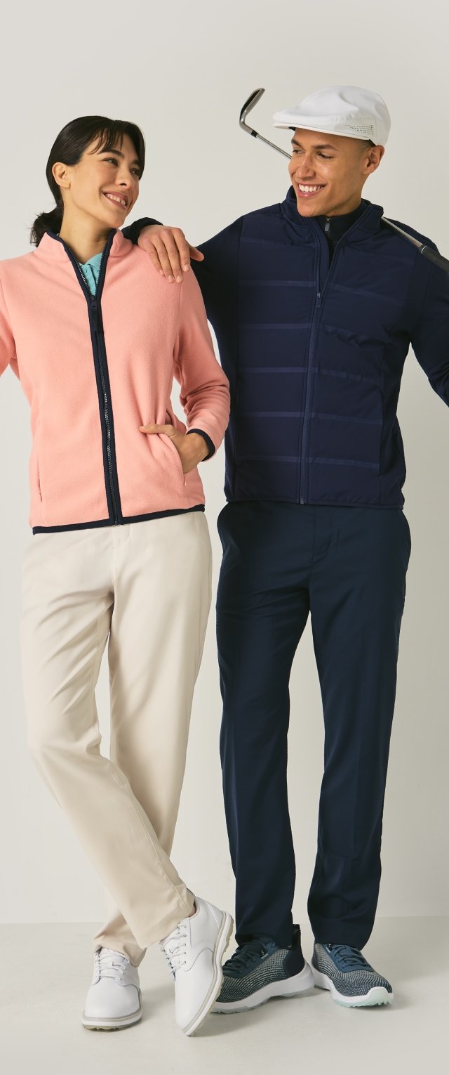 Dos personas llevan atuendos deportivos; la mujer con una chaqueta de forro polar rosa claro y pantalones crema, el hombre con una chaqueta azul marino y pantalones oscuros.