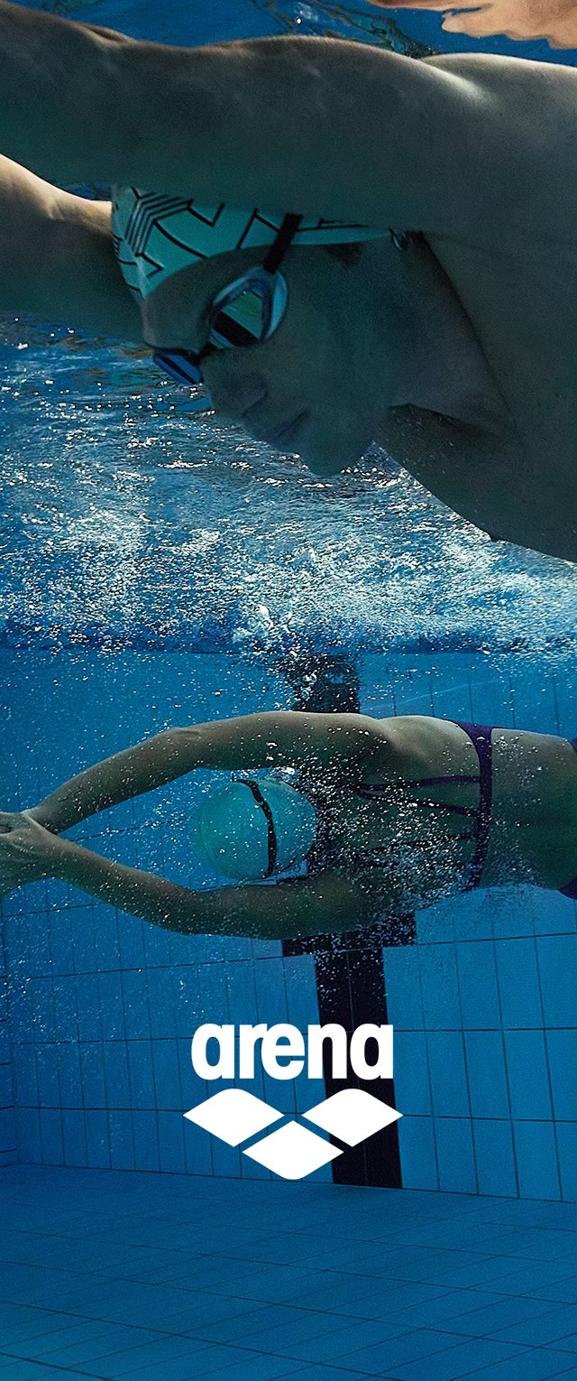 Dos nadadores bajo el agua en una piscina. Uno lleva un gorro de natación con estampado y gafas; el otro tiene un gorro liso. Los rodean azulejos azules y burbujas.