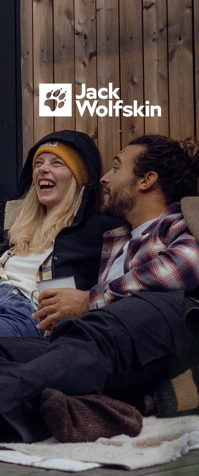 Deux personnes sont assises ensemble sur une couverture. L'une porte un bonnet jaune et un manteau sombre ; l'autre porte une chemise à carreaux et un pantalon noir.