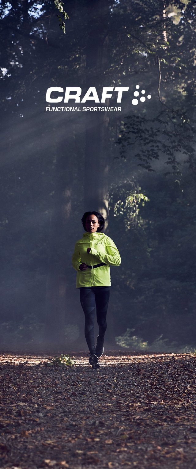 Heldere limoengroene waterdichte hardloopjack met rits, zwarte accenten, gecombineerd met zwarte leggings, in een bosachtige trailomgeving.