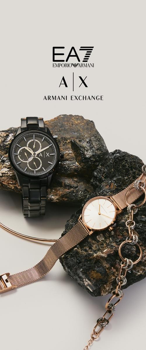Dos relojes de pulsera Armani—un cronógrafo negro y uno de malla en oro rosa—mostrados sobre rocas oscuras y texturizadas, con los logotipos de Armani Exchange arriba.
