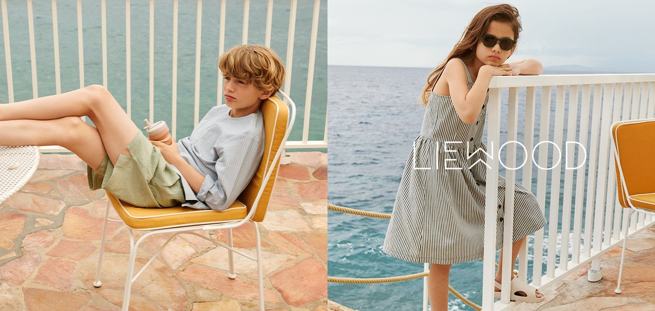 Pruhovaná modrá košile a zelené kraťasy na jednom dítěti, pruhované šaty na druhém. Oba oblečeni v neformálním letním oblečení, sedící u vody.