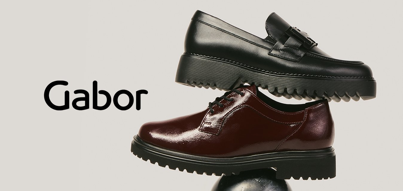 Černý kožený mokasín naskládaný nad tmavě hnědým lesklým oxfordským botou, oba vyvážené na kulaté černé mramorové kouli na jednobarevném pozadí.