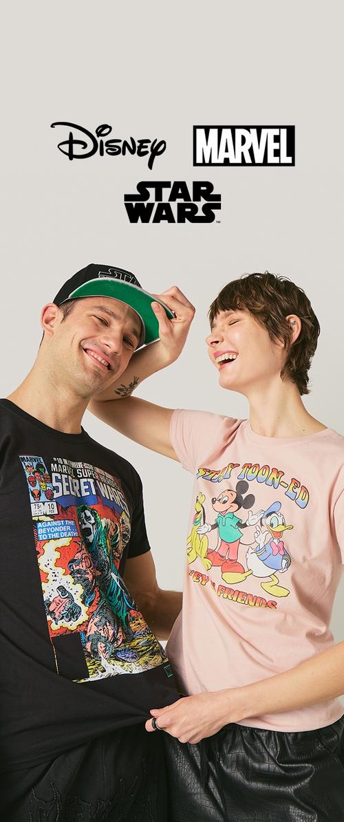 Hombre y mujer sonrientes con camisetas gráficas de Marvel y Disney Star Wars, la mujer ajusta juguetonamente la gorra de Star Wars del hombre sobre un fondo claro.