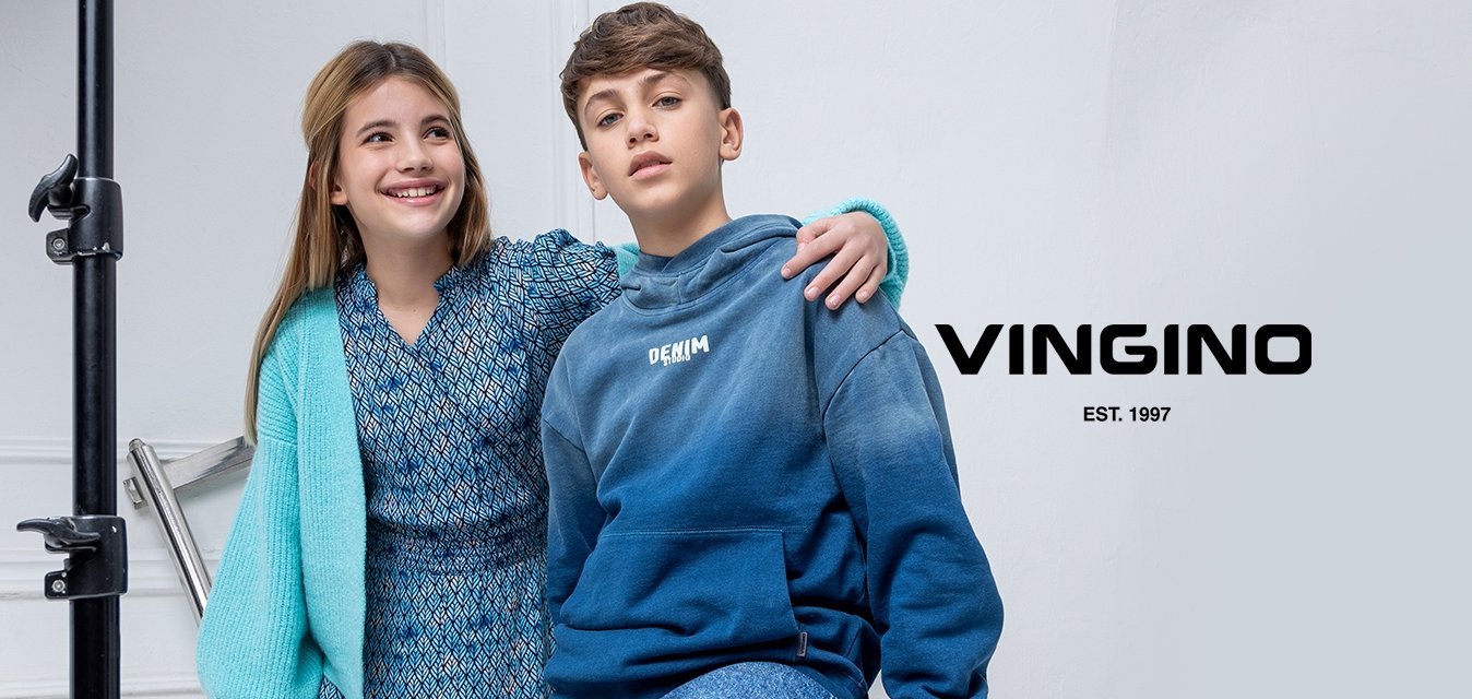 Dvě děti pózují ve studiu. Jedno má modré šaty s vzorem a světle modrý svetr, zatímco druhé má modrou mikinu s přechodem barev a džíny.