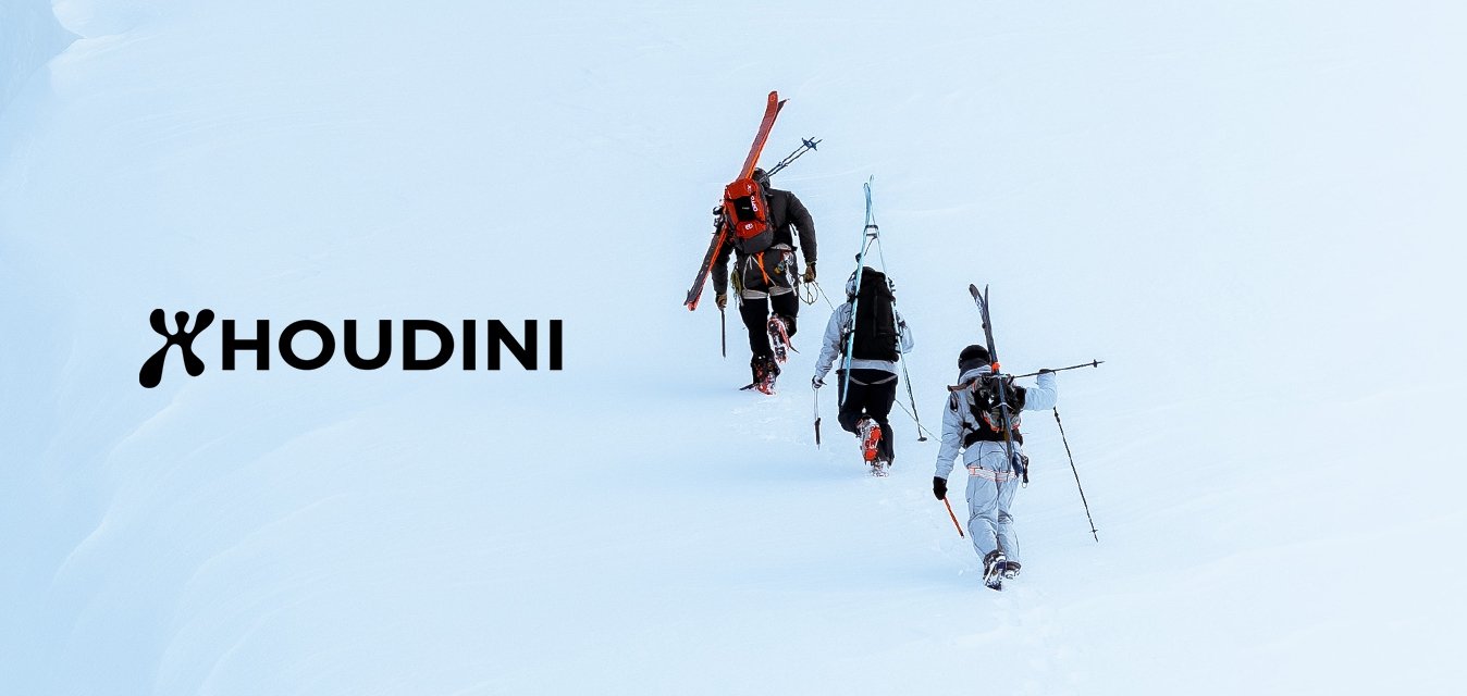 Tři lyžaři nesoucí lyže kráčí jeden za druhým napříč strmým zasněženým svahom blízko velké ledové trhliny.