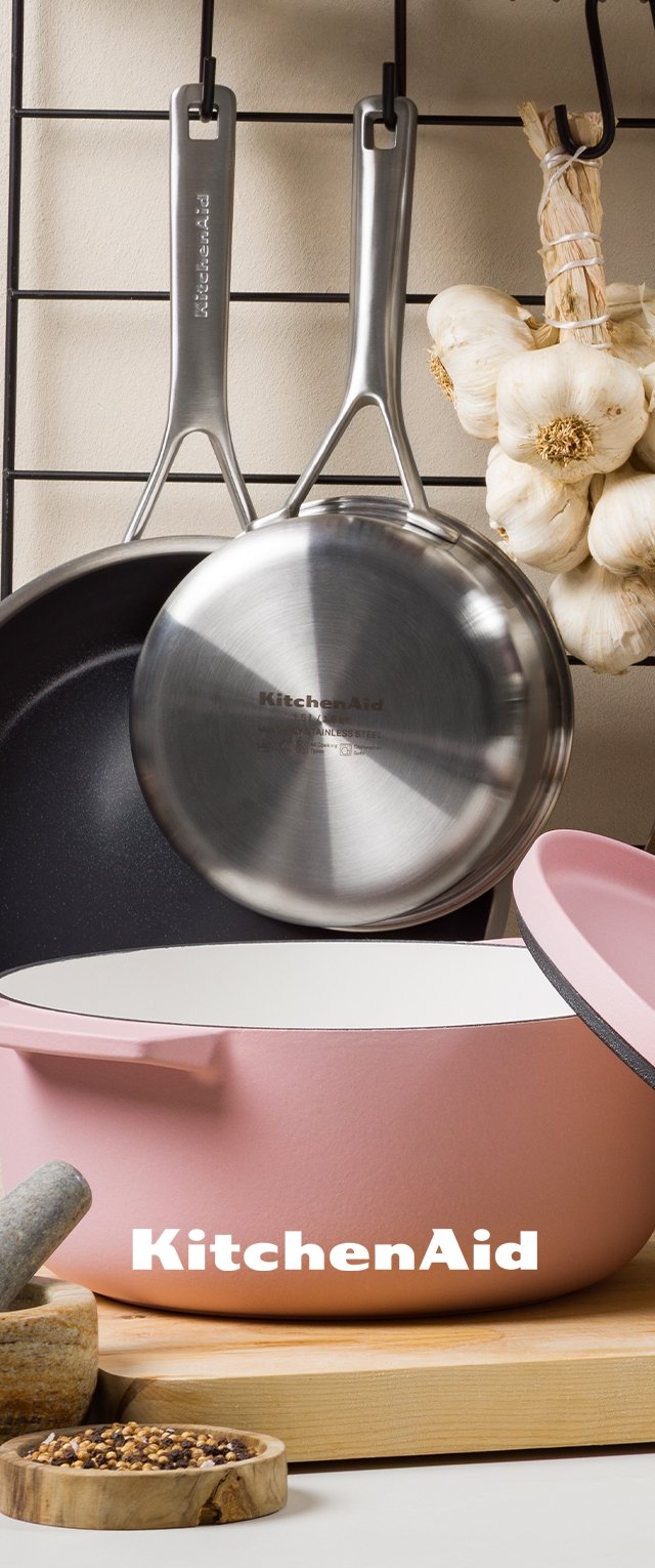 KitchenAid grytset som innehåller en rosa gryta med vit insida, en stekpanna i rostfritt stål med en blank yta, och vitlök hängande i bakgrunden.