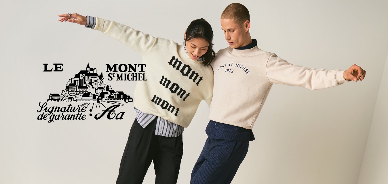 Dva lidé vyvažující se na dřevěné trámu uvnitř, oblečeni v běžných svetrech a kalhotách, s pažemi nataženými pro udržení rovnováhy.