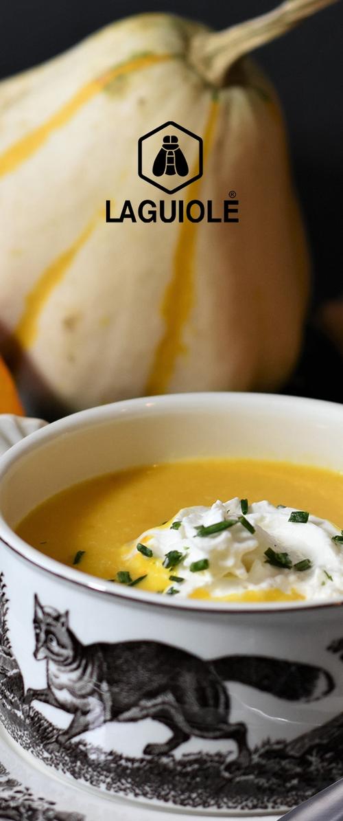 Cuenco de cerámica blanca con borde negro que presenta una ilustración de un zorro, lleno de una vibrante sopa amarilla, decorada con crema batida y cebollino.
