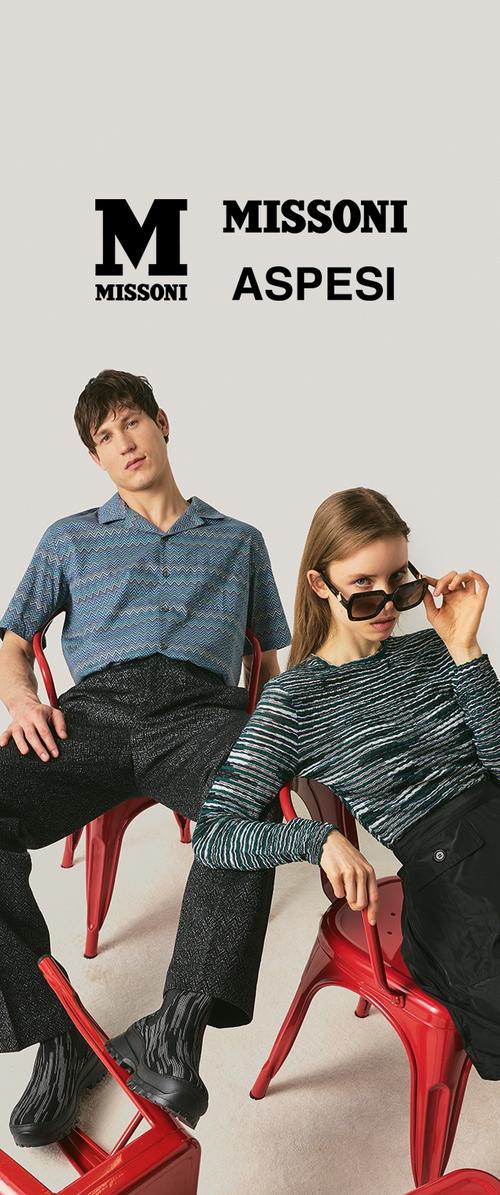 Due modelli seduti su sedie di metallo rosse, indossano maglie con motivi e pantaloni scuri, con i loghi dei marchi "MISSONI" e "ASPESI" sopra.