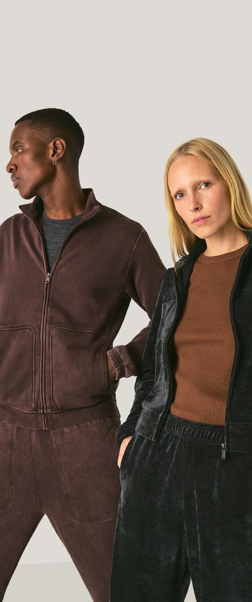 Deux personnes portant des survêtements en polaire assortis. L'une porte une veste et un pantalon marron foncé, l'autre en gris foncé avec une finition texturée.