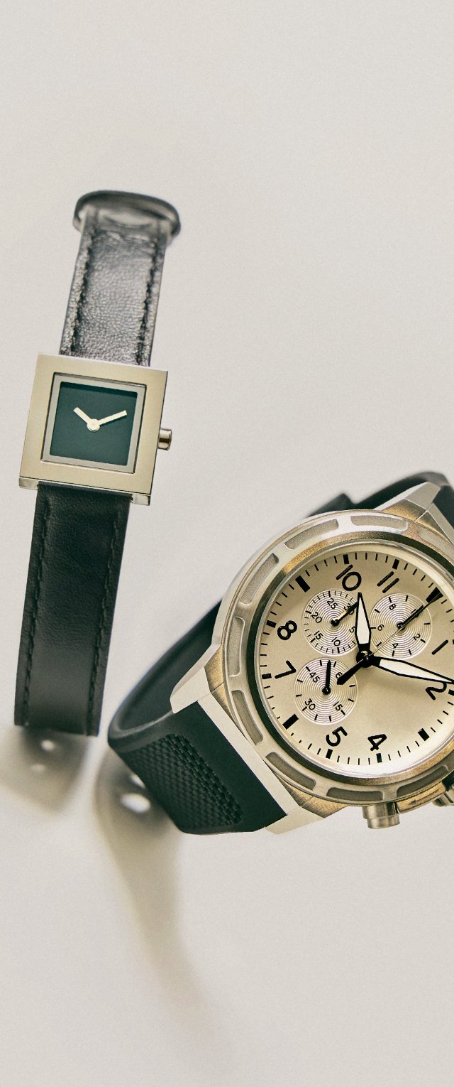 Due orologi da polso su una superficie bianca: uno con quadrante nero quadrato e cinturino in pelle, l'altro un cronografo tondo con ghiera argentata e cinturino in gomma nera.