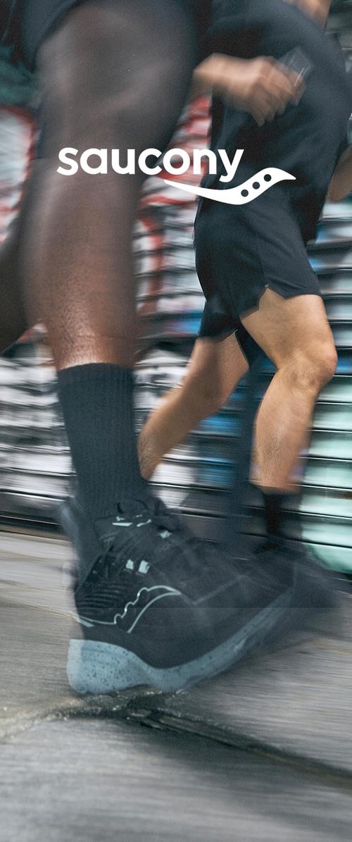 Schwarze Laufschuhe mit einer strukturierten Oberfläche und einer hellblauen gesprenkelten Sohle, in Bewegung festgehalten, vor einem verschwommenen Hintergrund.