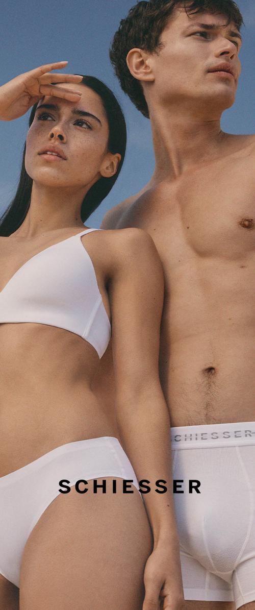 Donna e uomo con biancheria intima bianca posano contro un cielo azzurro limpido, donna si protegge gli occhi con la mano, nome del marchio Schiesser visibile in vita.