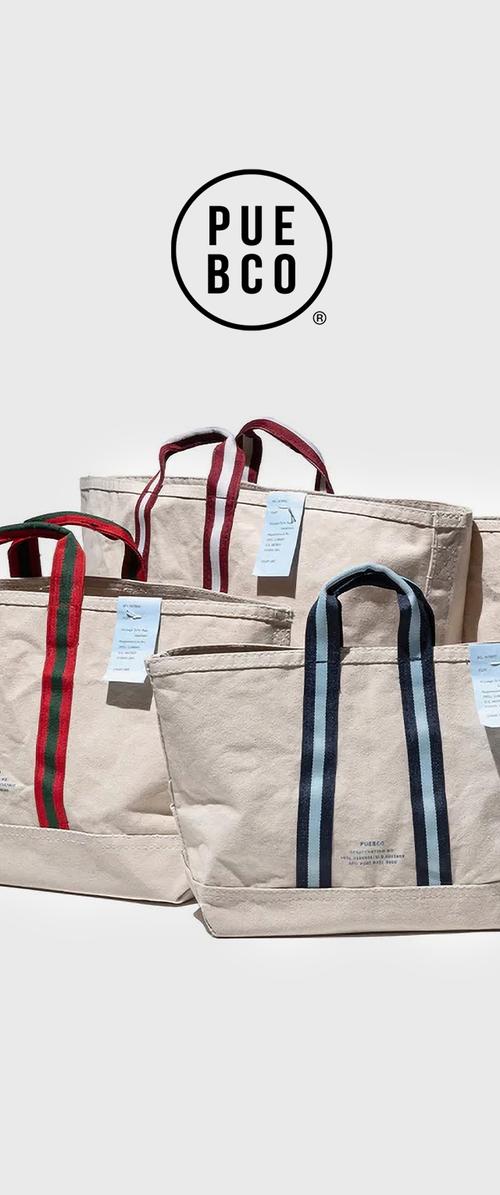 Katoenen totebags in beige met contrasterende gestreepte handvatten: rood, marineblauw en donkerblauw. Labels bevestigd met het merklogo en details.