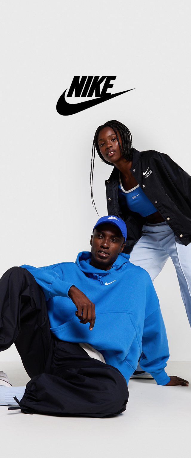 Sudadera azul con bolsillo frontal y logo blanco, combinada con pantalones negros. Modelo vistiendo chaqueta negra y top azul. Fondo simple.