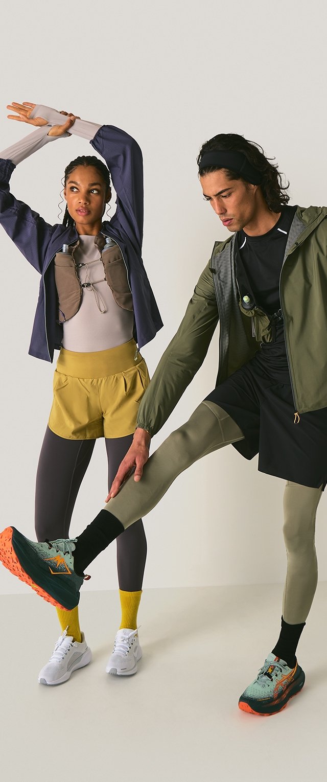 Dos atletas en ropa deportiva: uno lleva una chaqueta gris, pantalones cortos amarillos y mallas; el otro lleva una chaqueta verde, pantalones cortos negros y mallas grises.