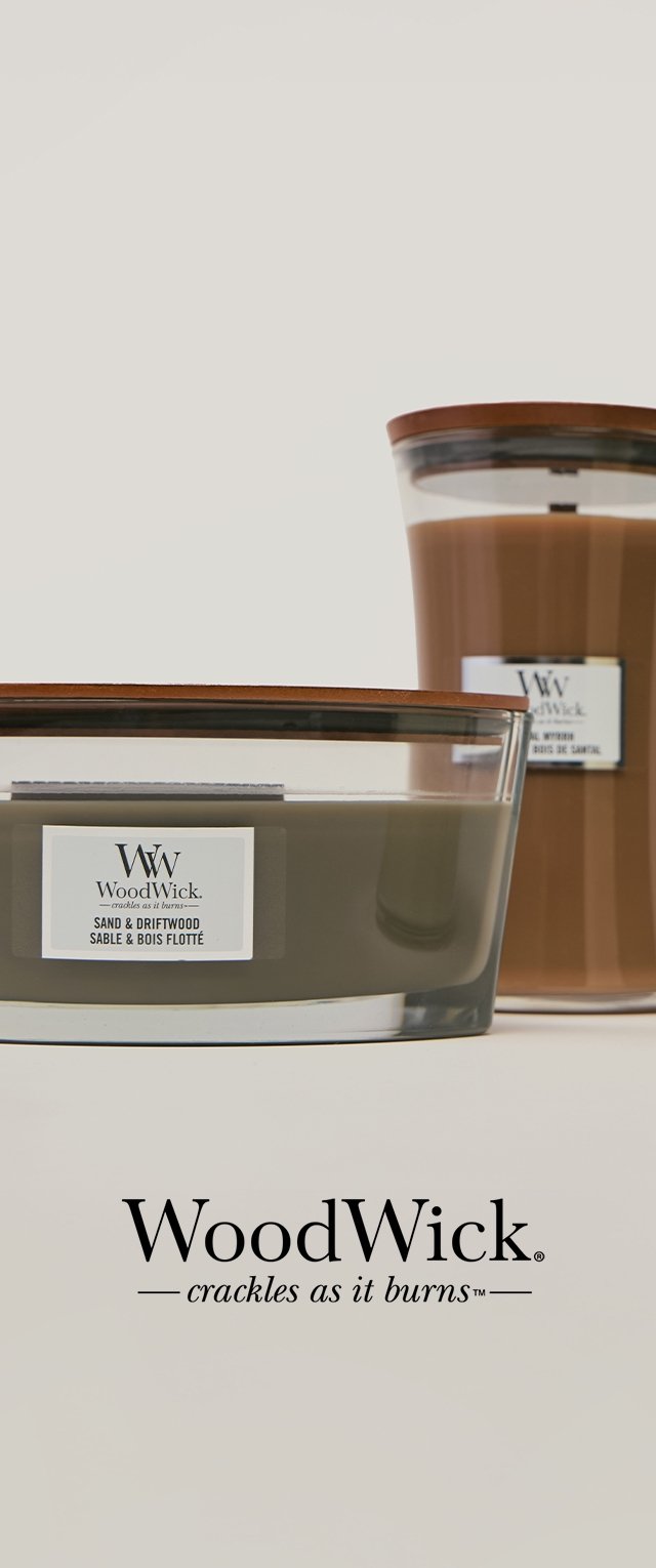 Two WoodWick candles with wooden lids, labeled Sand & Driftwood; text "WoodWick crackles as it burns" below on light background.