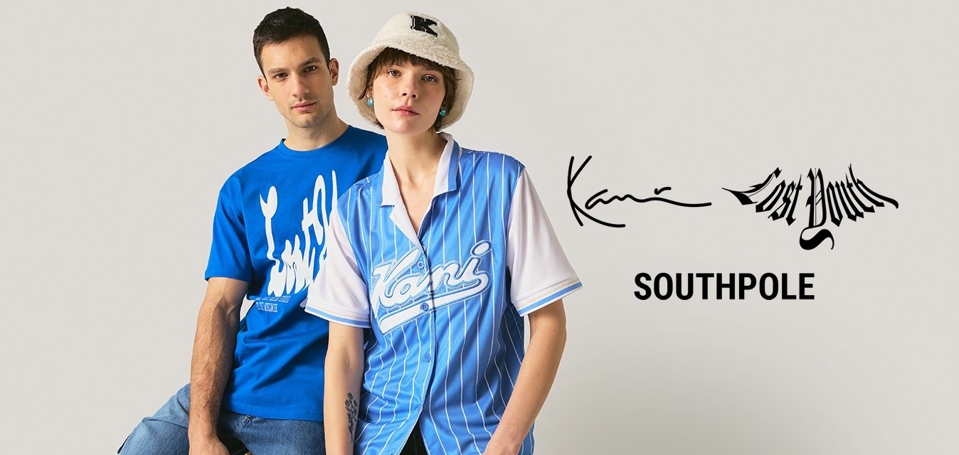 Mladý muž v modrém tričku s grafikou a mladá žena v modré pruhované košili a bílém klobouku stojí před jednobarevným pozadím.