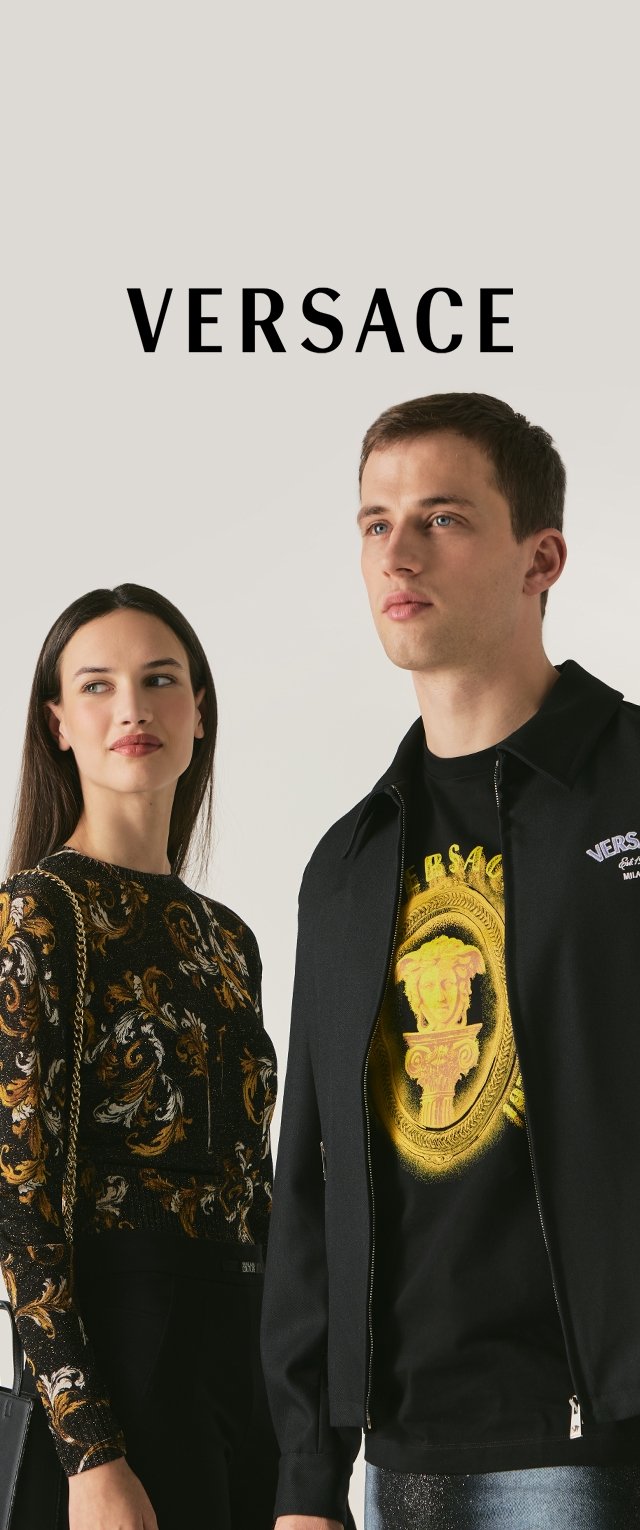 Giacca nera con cerniera e logo ricamato, abbinata a una t-shirt nera con grafica dorata. Donna con top a maniche lunghe a fantasia.