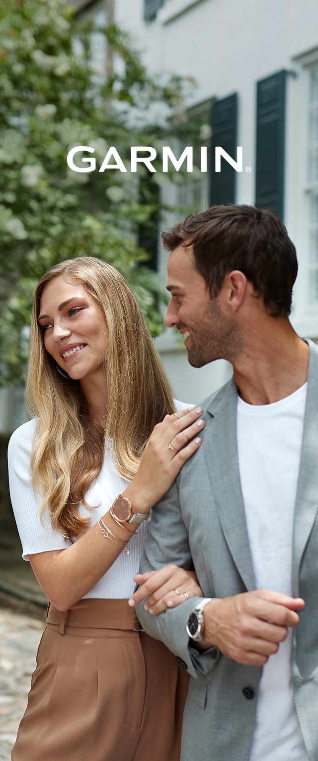 Due persone indossano orologi Garmin. La donna ha i capelli lunghi e mossi, indossa una maglietta bianca e pantaloni beige; l'uomo ha un blazer grigio e una camicia bianca.