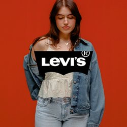 Mladá žena v lehkém topu a džínách částečně svléká modrou denimovou bundu, stojící před jednobarevným oranžovým pozadím, zavřenýma očima.