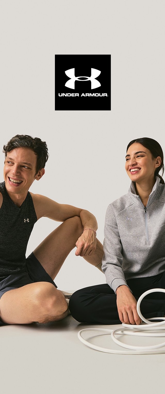 Dos personas se sientan sobre un fondo claro. Una lleva un top sin mangas negro y pantalones cortos; la otra viste una chaqueta gris con cremallera. Hay aros blancos de ejercicio presentes.