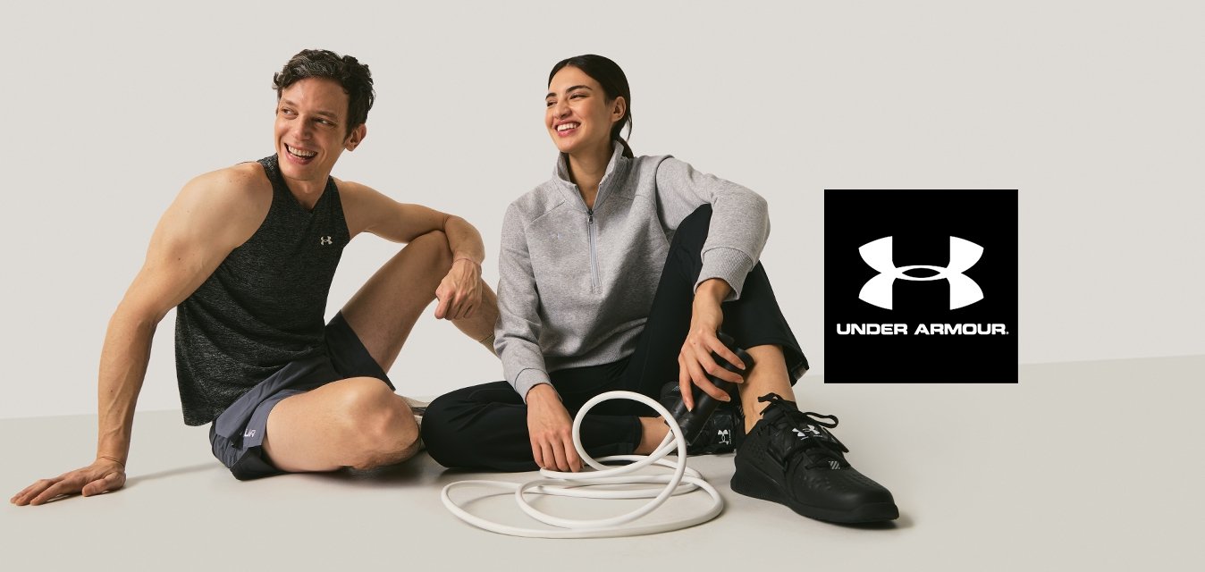 Dva dospělí v atletickém oblečení sedící na podlaze a usmívající se, mezi nimi stočené bílé cvičební lano, na jednobarevném pozadí.