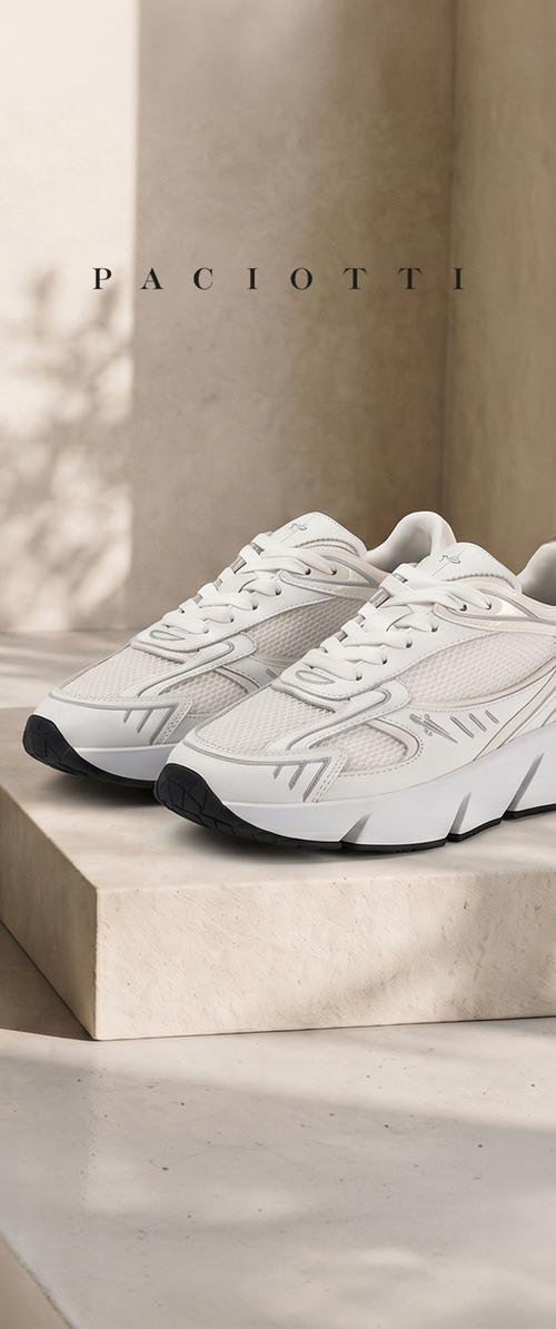 Un par de zapatillas Paciotti blancas de malla y suela gruesa, expuestas sobre un pedestal de piedra.